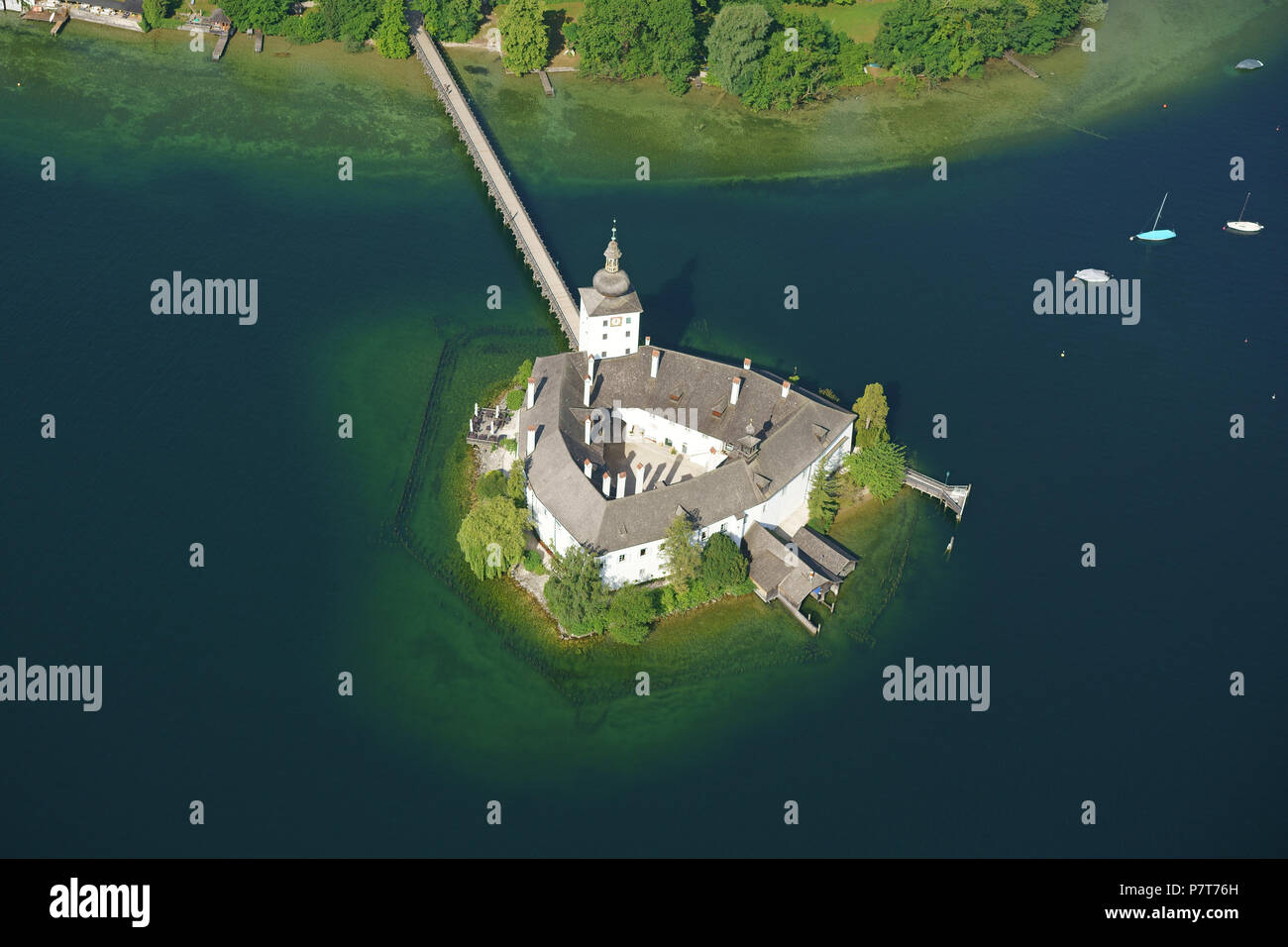 VISTA AEREA. Castello medievale su un lago con un ponte pedonale per l'accesso. Castello di Ort, Gmunden, Traunsee (lago), Austria superiore, Austria. Foto Stock