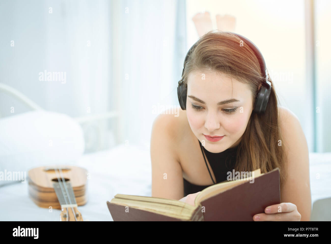 Ragazza distesa sul letto libri di lettura e ascolto di musica sulle cuffie per rilassarsi. Foto Stock