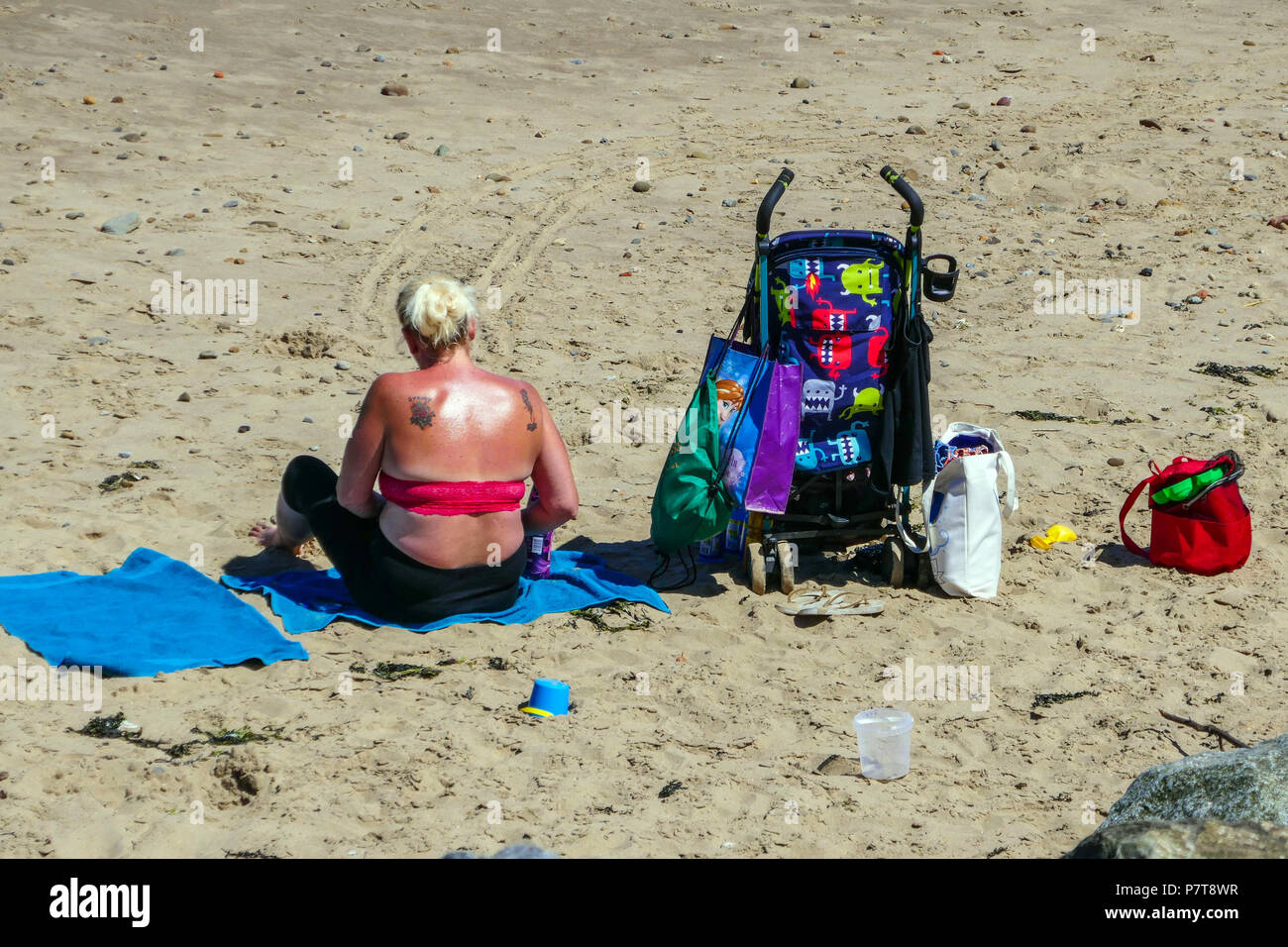 Donna obesa sulla spiaggia con passeggino blu caldo giorno d'estate come cittadina balneare di Skinningrove, North Yorkshire Foto Stock