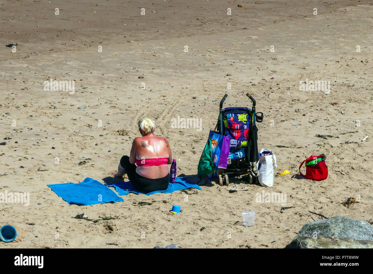 Donna obesa sulla spiaggia con passeggino blu caldo giorno d'estate come cittadina balneare di Skinningrove, North Yorkshire Foto Stock