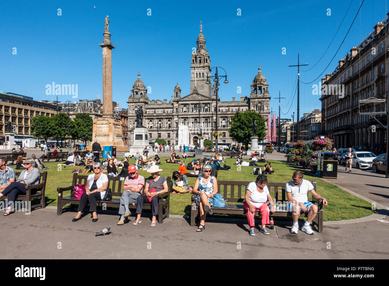La gente fuori a godersi una piacevole serata di sole in George Square, Central Glasgow, con la City Chambers in background, il Cenotafio, e statue, Foto Stock