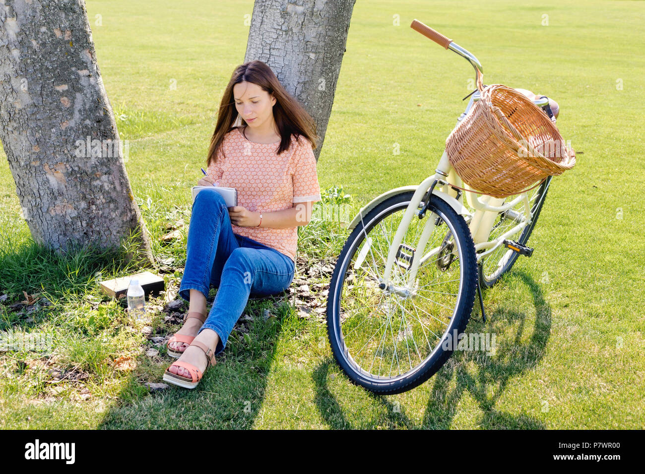 Immagine di donna giovane studente scrive in un notebook seduto sotto un albero in un giorno di estate Foto Stock