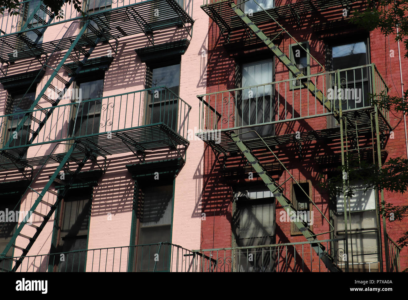 Chiudere fino a due vecchi edifici in mattoni di Lower Manhattan dipinta in rosa e rosso, con fuoco verde sfugge che gettano ombre interessanti sulla loro facciate Foto Stock