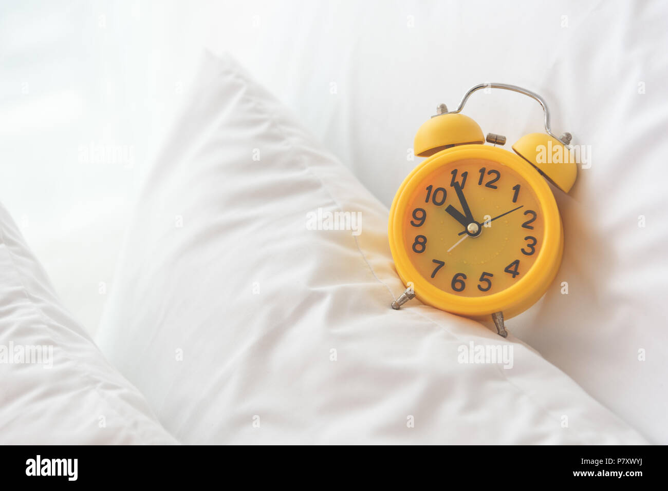 Allarme giallo di clock sul letto bianco sullo sfondo. Viaggi e Vacanze concetto. Home accessori oggetto del tema. Foto Stock