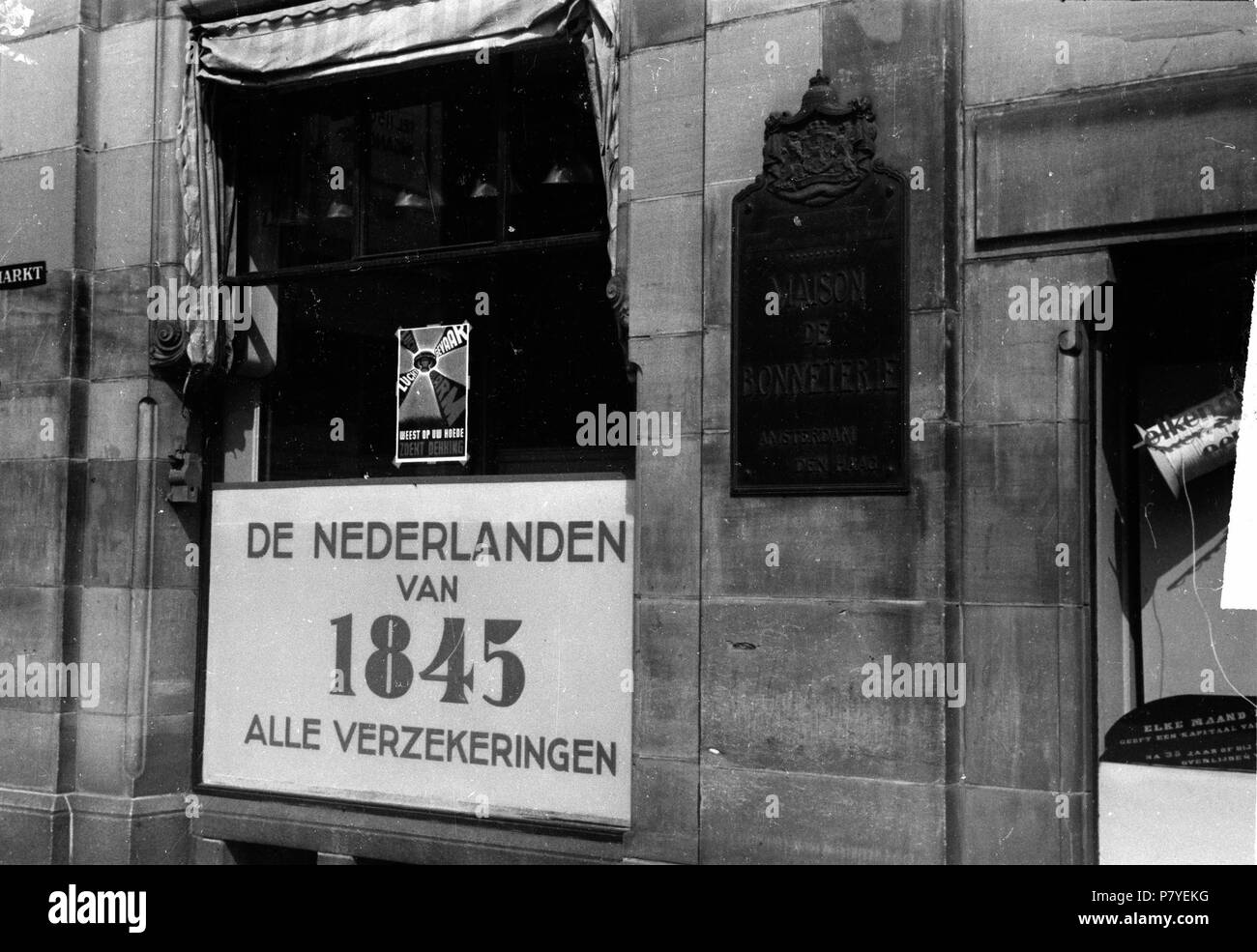 . Huizinga collectie etalages Den Haag - NIOD - 216363. Nederlands: Foto uit de collectie Huizinga van het NIOD. Naambord van verzekeringsmaatschappij, dat in het pand van de Bonnetterie era ondergebracht onder een affiche:Luchtgevaar. Wees op uw hoede. Zoekt dekking! Menno Huizinga era onderdeel van de Ondergedoken fotocamera en maakte illegaal foto tijdens de bezetting. Dit deed hij hoofdzakelijk in zijn woonplaats Den Haag (L'Aia). Data sconosciuta 36 BC856 HUI-1054 Foto Stock