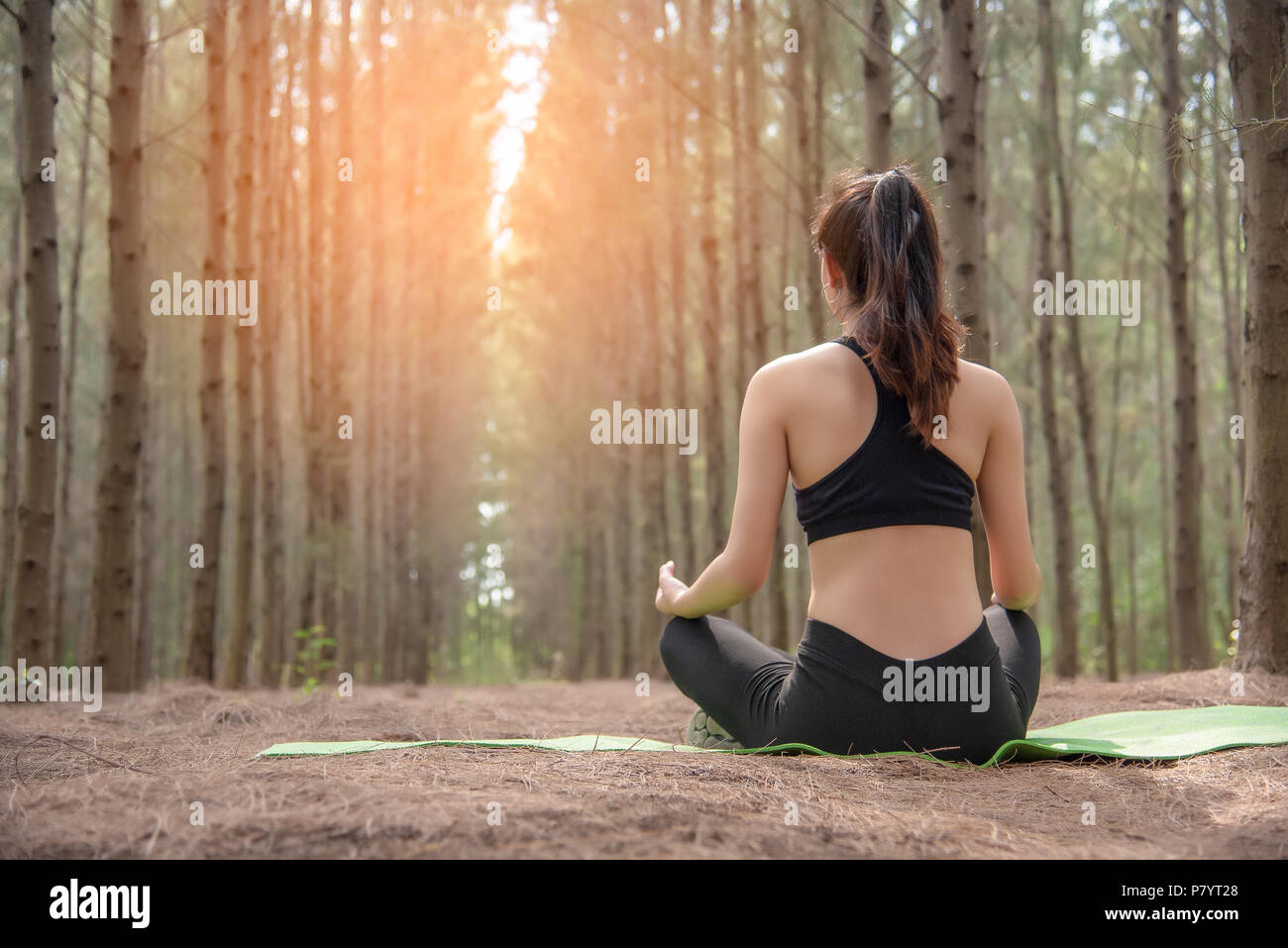Bella asiatica giovane donna sdraiata sul tappeto verde e fare yoga nella foresta. Esercizio e concetto di meditazione. Tranquillo e concetto di campagna. In legno di pino Foto Stock