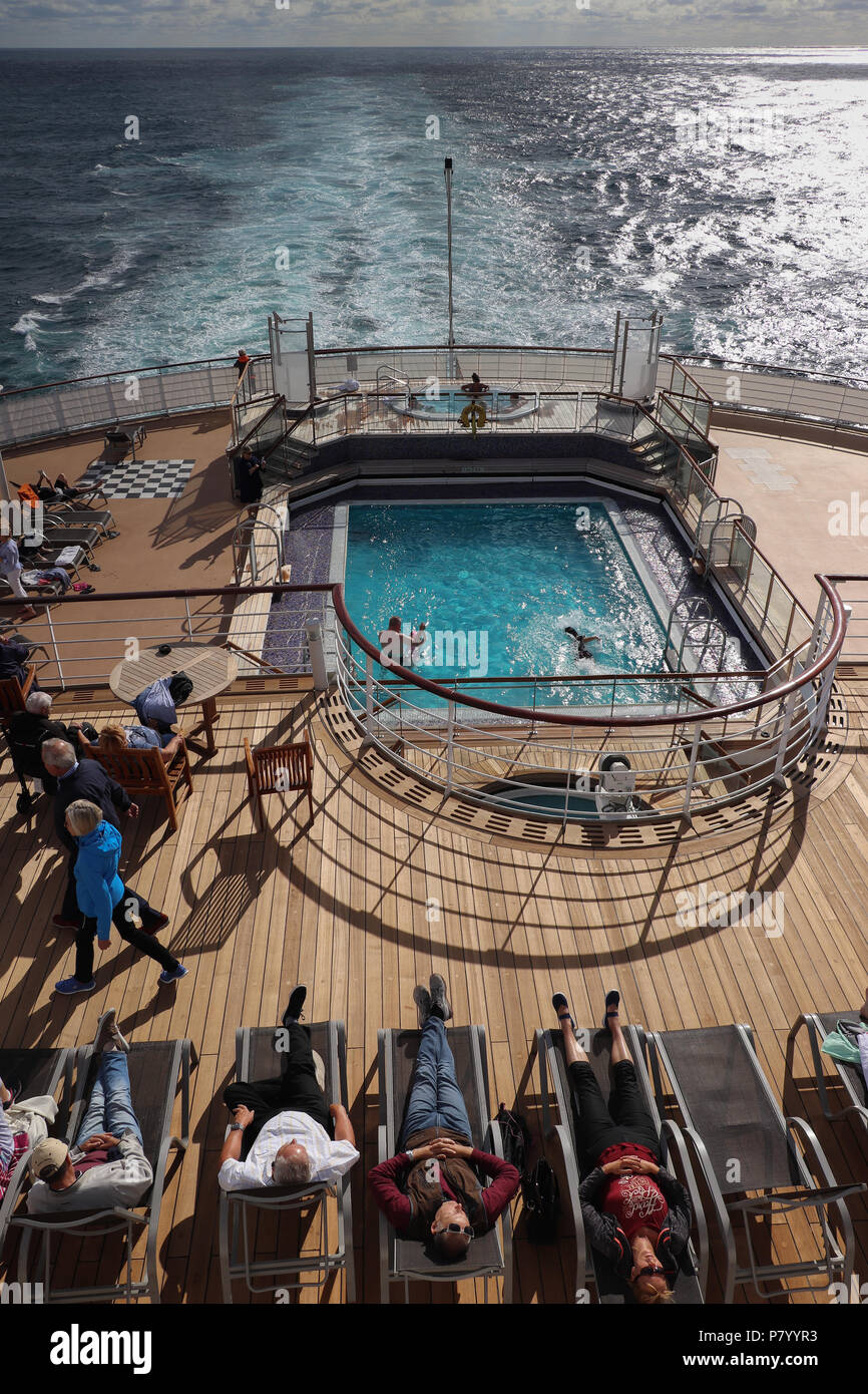 Guardando verso il basso sul ponte 7 sulla poppa della Queen Mary 2 in un pomeriggio soleggiato, con persone sole se stessi o il nuoto in piscina come la nave a vela. Foto Stock