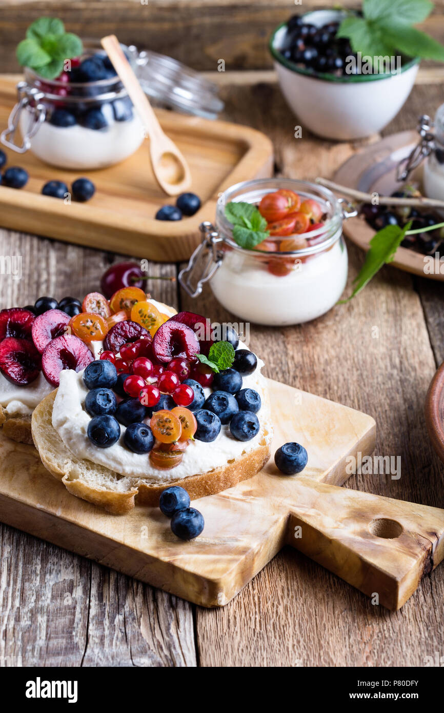 La crema di formaggio panini e cheesecake parfait di color crema con fresca frutta estiva in vaso e sana prima colazione Foto Stock