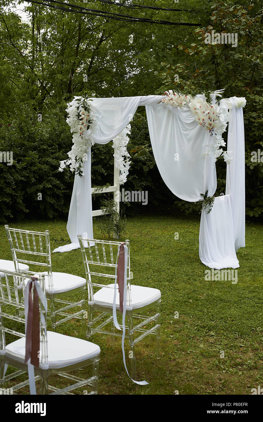 Cerimonia di matrimonio all'aria aperta.sedie trasparenti con nastri  svolazzanti nel parco o sulla foresta. Arch decorate con il bianco di  chiffon e fiori Foto stock - Alamy