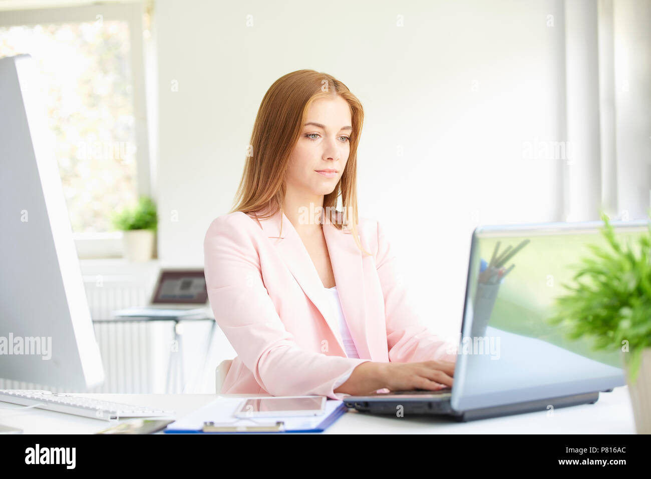 Ritratto di giovane e bella imprenditrice seduta presso un ufficio moderno e di lavoro sul computer portatile. Foto Stock