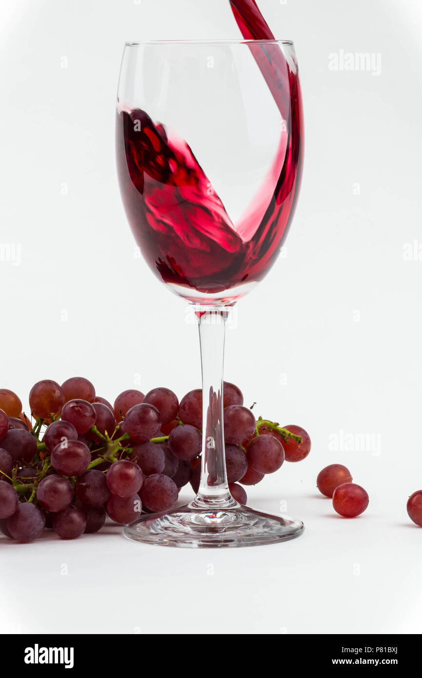 Vino rosso versato in un bicchiere con uve fresche come sfondo. Foto isolate. Foto Stock