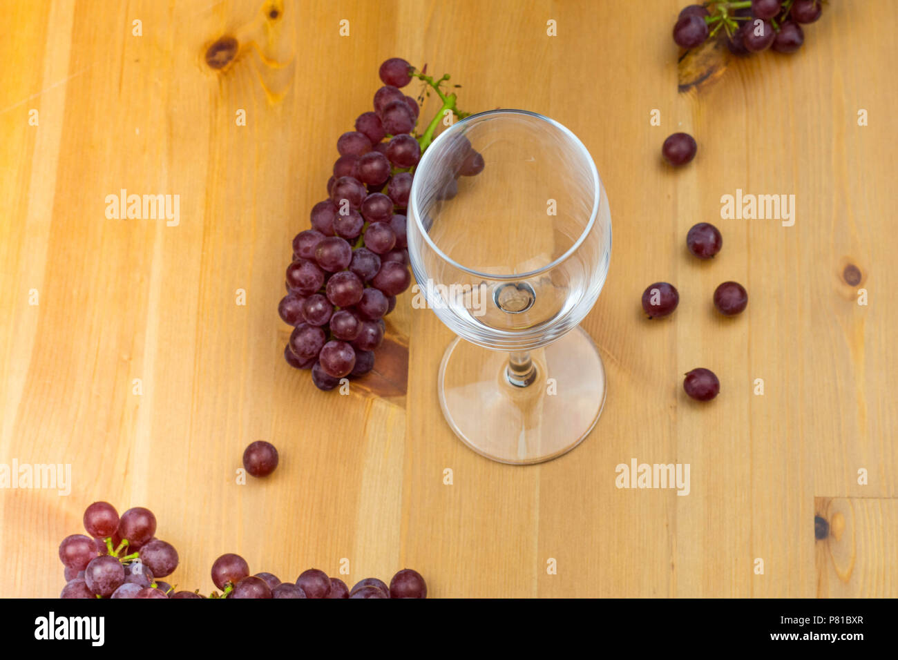 Svuotare il vino rosso del vetro su di un tavolo di legno con uve fresche sparsi in background come design Foto Stock