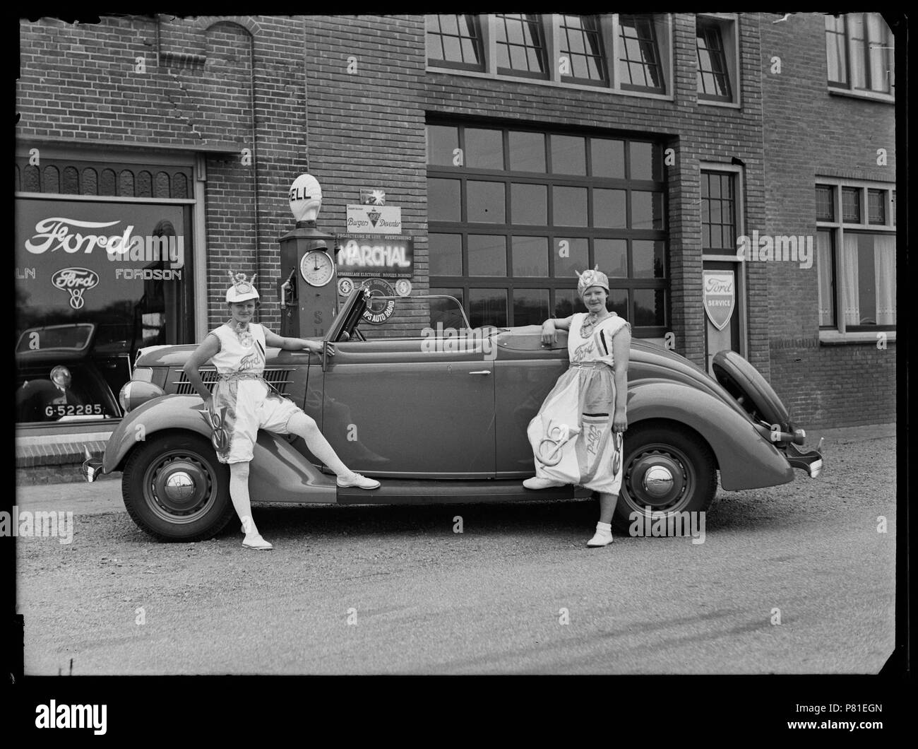 Garage Ford ha incontrato i fasti della Shell, van Maarten Smit in de Blauwe Keet, een gehucht verdwenen langs het Noordhollandsch Kanaal, nabij Julianadorp. Voor de garage een personenauto met twee vrouwen in kostuum voor een reclame actie Julianadorp 1930 Catalogusnummer: RAA003012812 Collectie Regionaal Archief Alkmaar . 12 ottobre 2011, 21:15 160 Ford garage (30512977344) Foto Stock