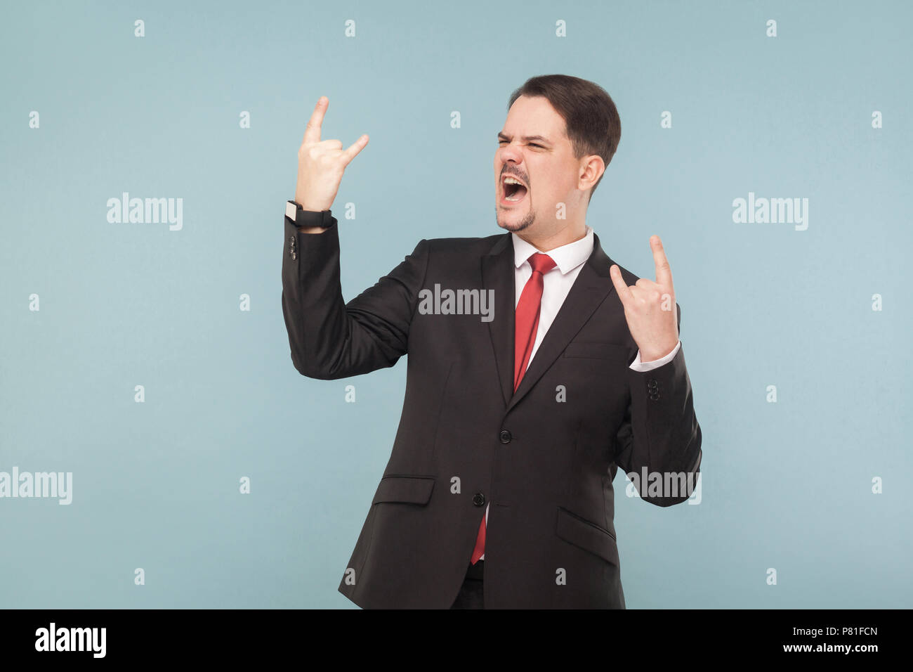 La felicità uomo attraente nel classico di usura preferiti ascolta rock band e canta con themIndoor . piscina studio shot. isolato su fondo azzurro. Foto Stock