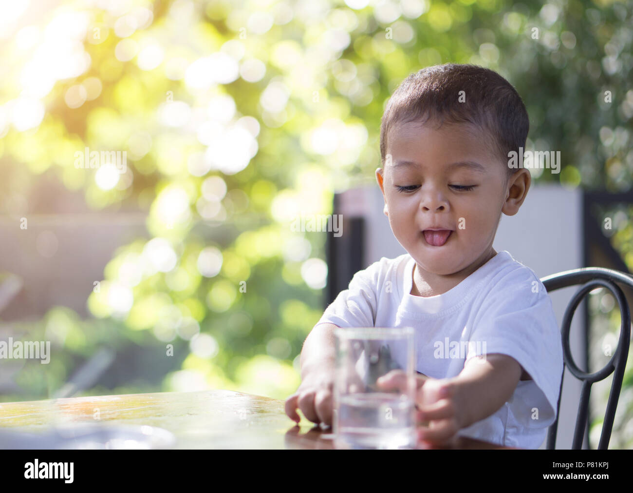 Piccolo bambino asiatico di andare a bere acqua in un bicchiere di vetro alla mattina il tempo con la natura bokeh sfondo. Foto Stock
