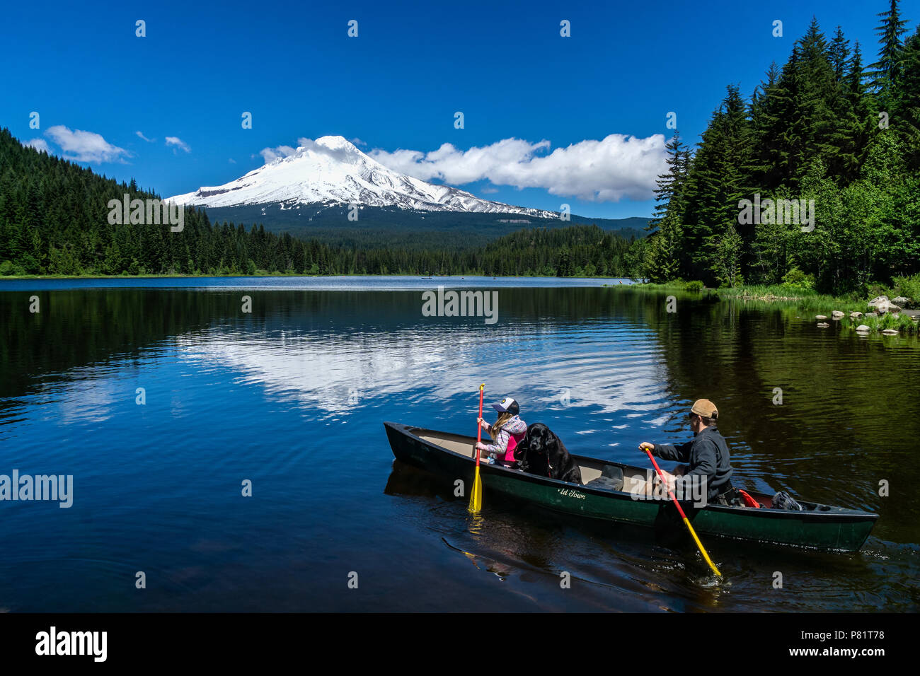 Padre e figlia con il loro cane andare in canoa sul lago Trillium su una bella giornata di sole dell'estate con Mt. Il cofano riflettendo sull'acqua, Oregon, Stati Uniti d'America. Foto Stock