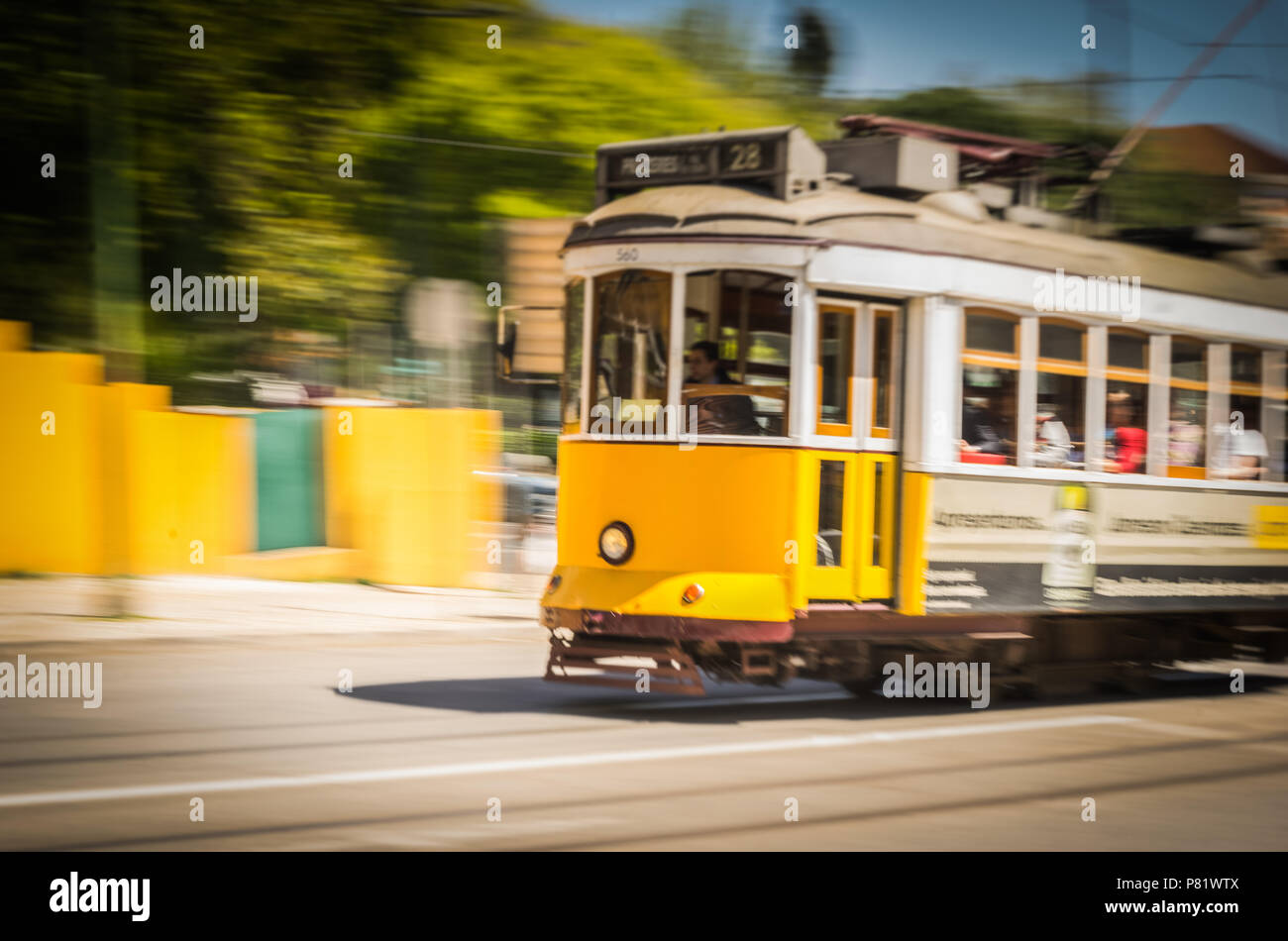 Storico tram giallo di Lisbona in movimento con passeggeri a bordo, che mostra il tradizionale trasporto in tram elettrico in Portogallo. Foto Stock
