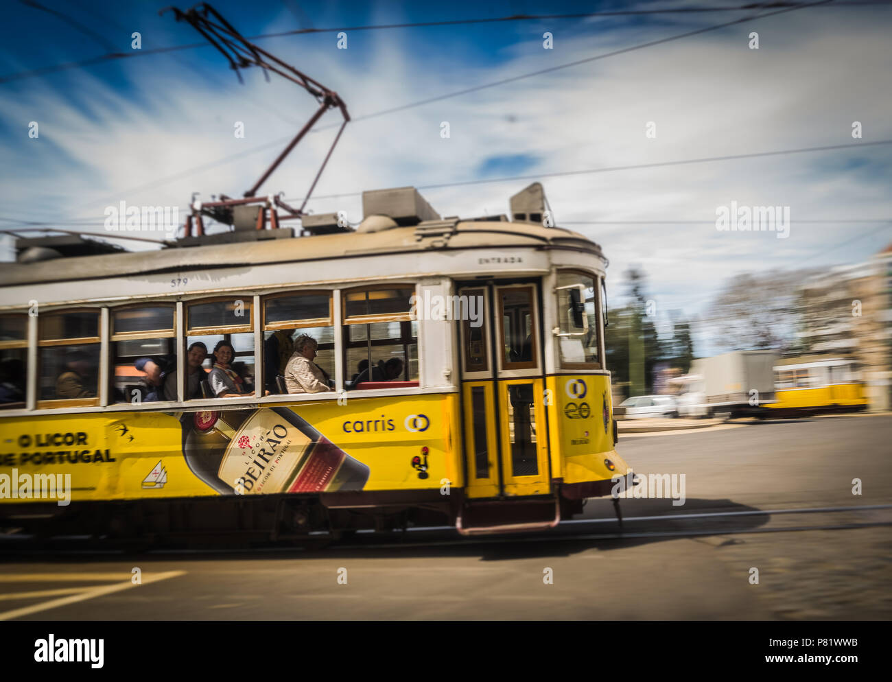 Storico tram giallo di Lisbona in movimento con passeggeri a bordo, che mostra il tradizionale trasporto in tram elettrico in Portogallo. Foto Stock