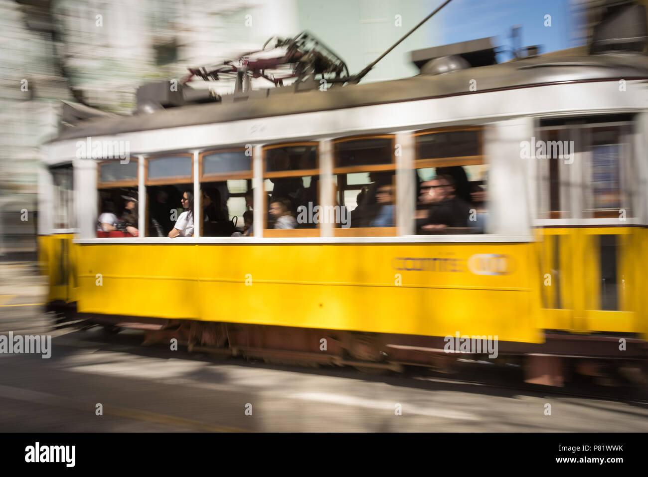 Storico tram giallo di Lisbona in movimento con passeggeri a bordo, che mostra il tradizionale trasporto in tram elettrico in Portogallo. Foto Stock