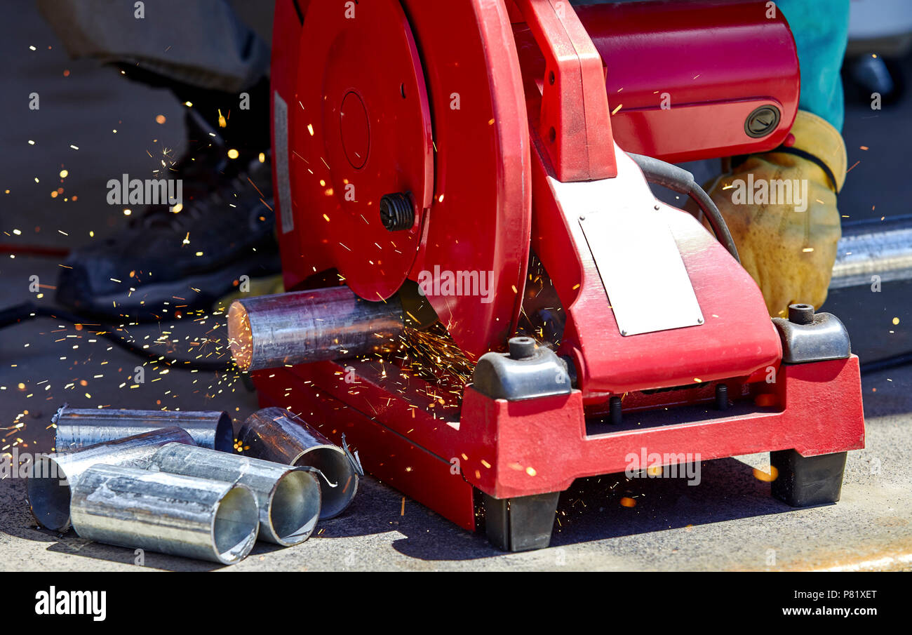 Un lavoratore edile il taglio di un acciaio zincato tubo con una troncatrice troncatrice Foto Stock