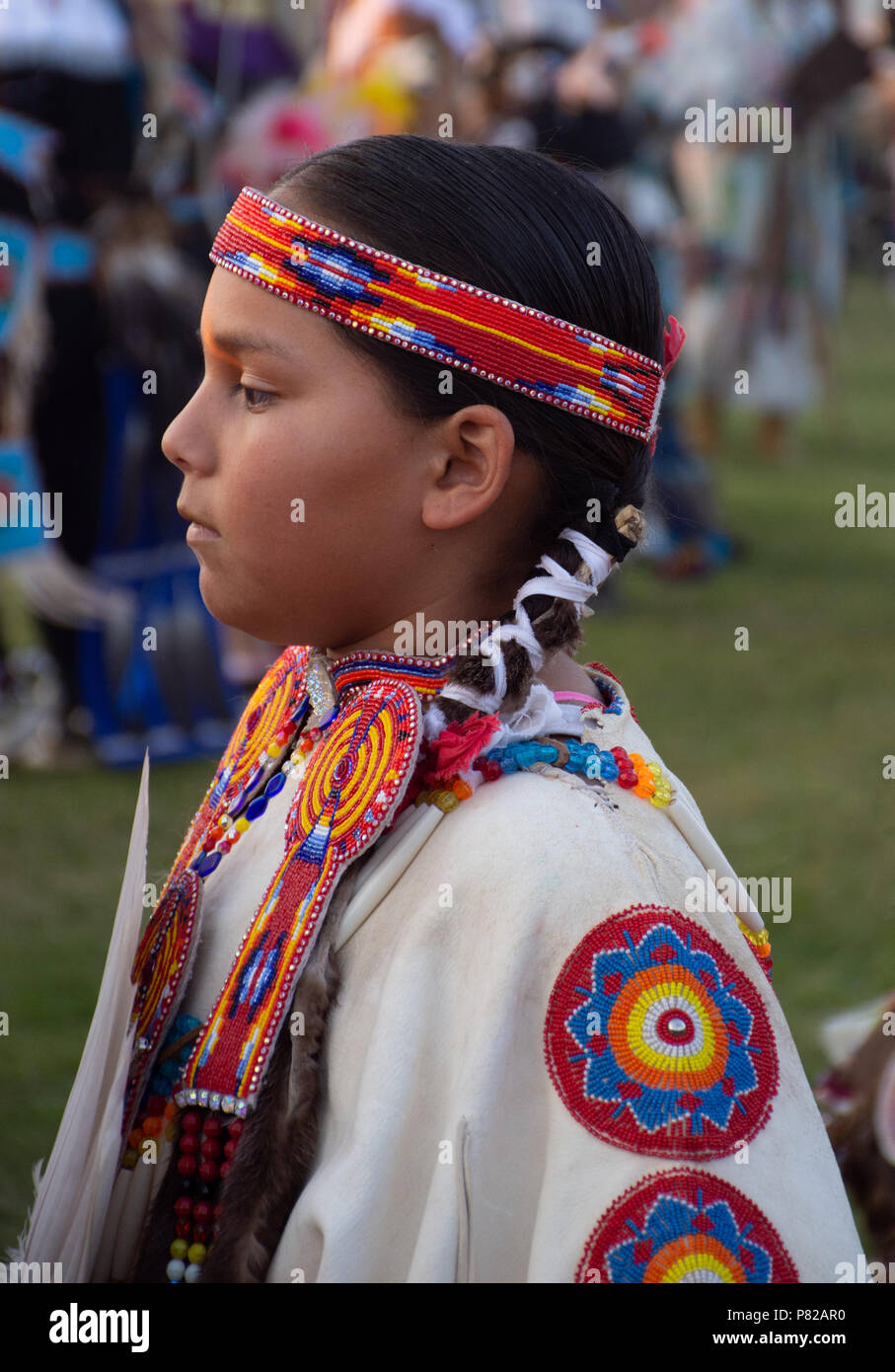 Close up di un nativo americano bambina indossa un abito bianco con rosso, blu, arancione, giallo e bianco bordato medaglioni e un archetto a perline. Foto Stock Close up di un nativo americano bambina indossa un abito bianco con rosso, blu, arancione, giallo e bianco bordato medaglioni e un archetto a perline. Foto Stock