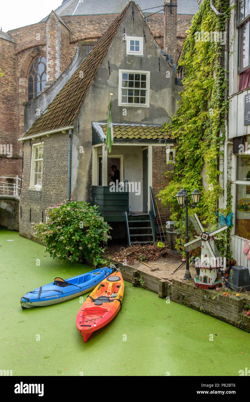 Una delle case più antiche di Delft lungo il canale Vrouwenrecht. Due canoe in acqua e un piccolo mulino a vento nel giardino Foto Stock