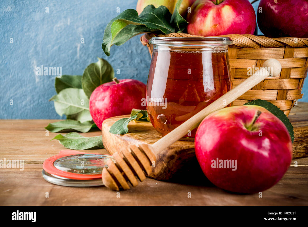 Festa ebraica di Rosh Hashanah o apple festa concetto, con le mele rosse, foglie di apple e il miele in barattolo, luce blu e lo sfondo di legno spazio copia Foto Stock