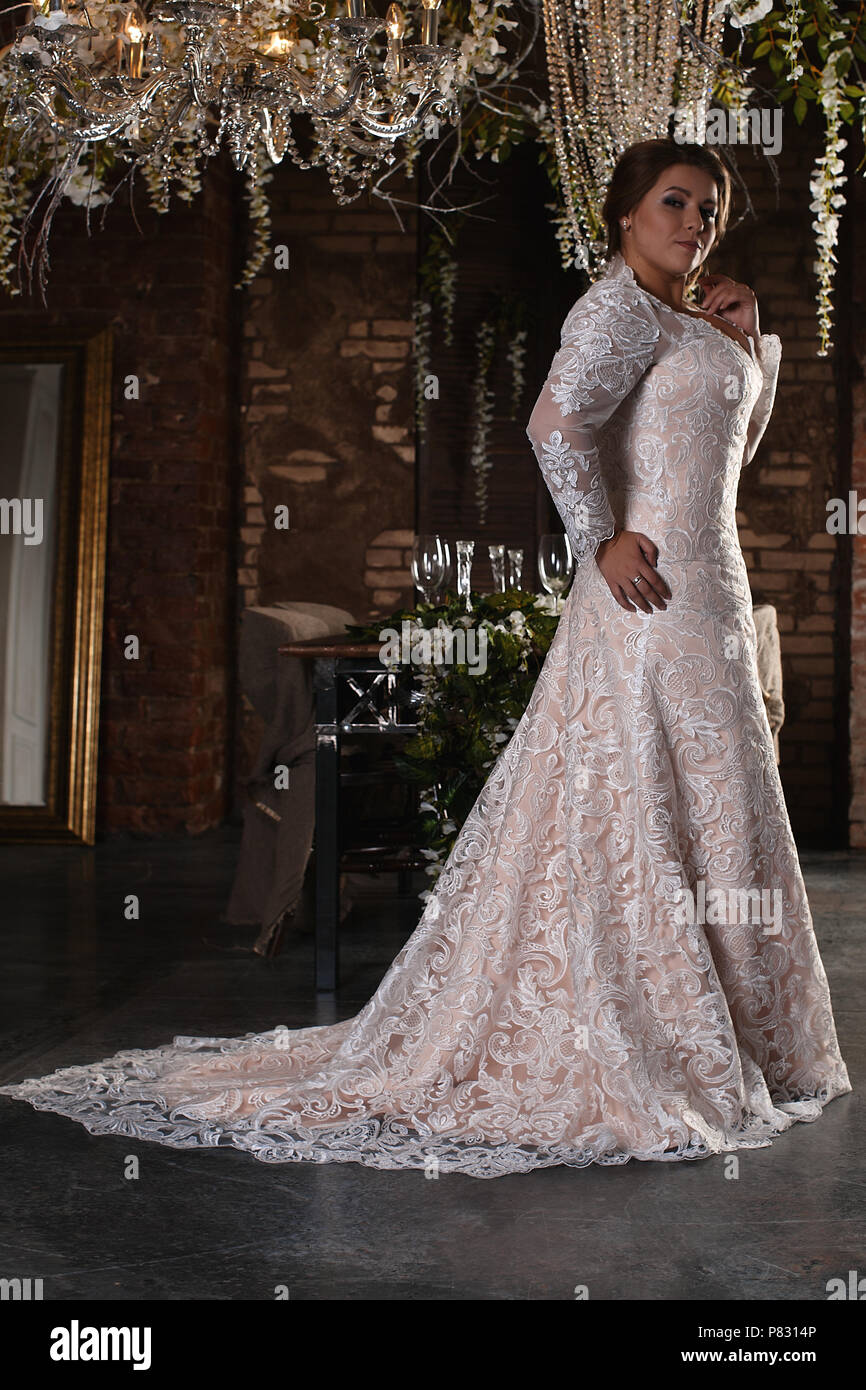 Ritratto di una bella sposa. Abito in pizzo. Matrimonio acconciatura e il trucco. Il labbro di brillanti colori. Fiori sul lato. La romantica atmosfera della sposa Foto Stock