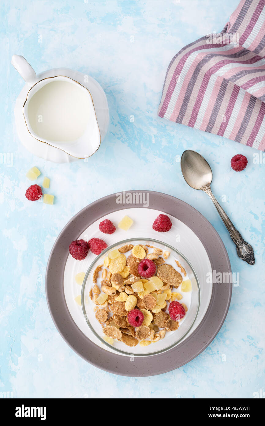 Grano intero fiocchi, lamponi, frutta e latte sulla luce tabella blu. Mangiare sano e sana colazione concetto. Vista superiore, verticale. Foto Stock