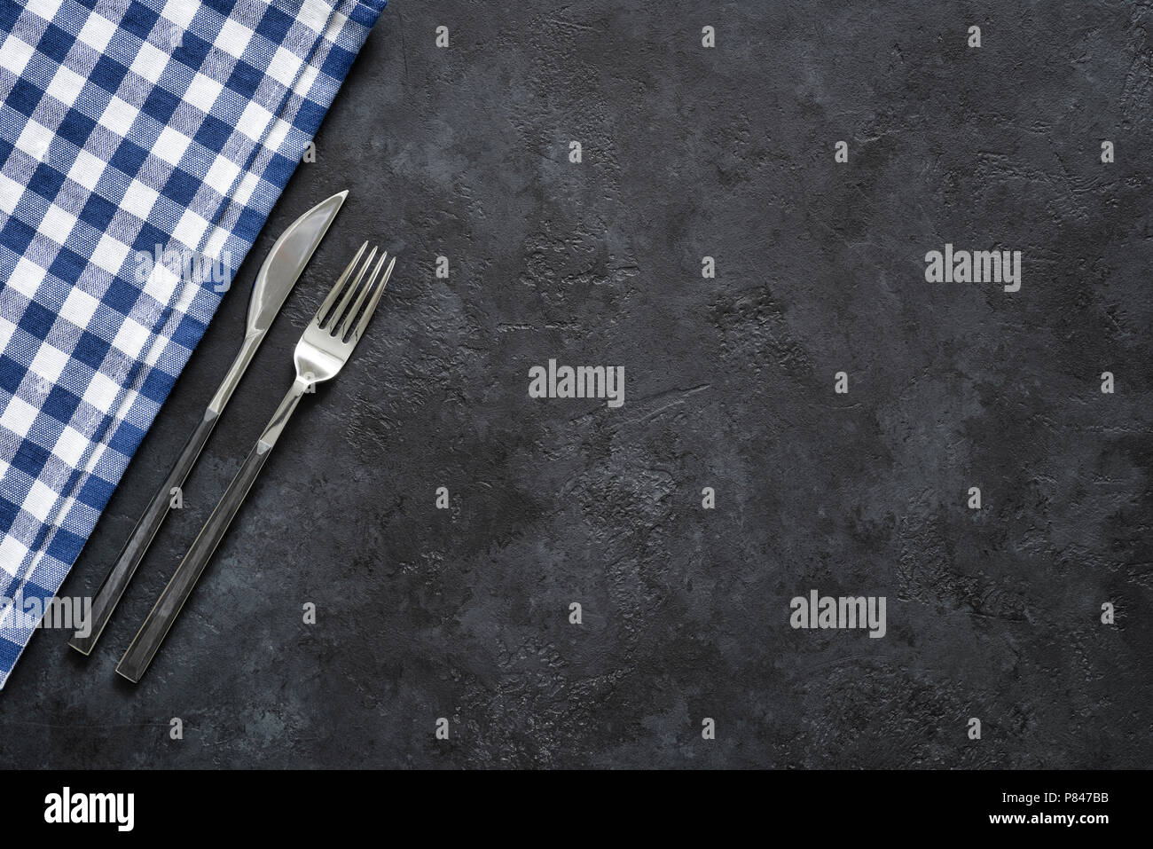 Impostazione tabella con argenti e prodotti tessili sul calcestruzzo nero Posate moderne, forchetta e coltello. Ristorante argenteria. Vista da sopra con copia spazio per il testo Foto Stock