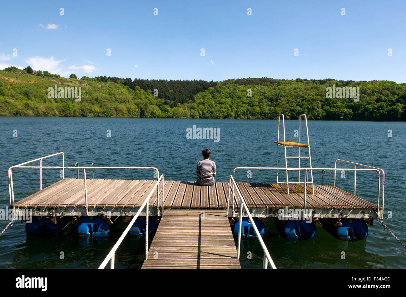 Donna seduta su un pontone affacciato su un lago, Auvergne, Francia Foto Stock