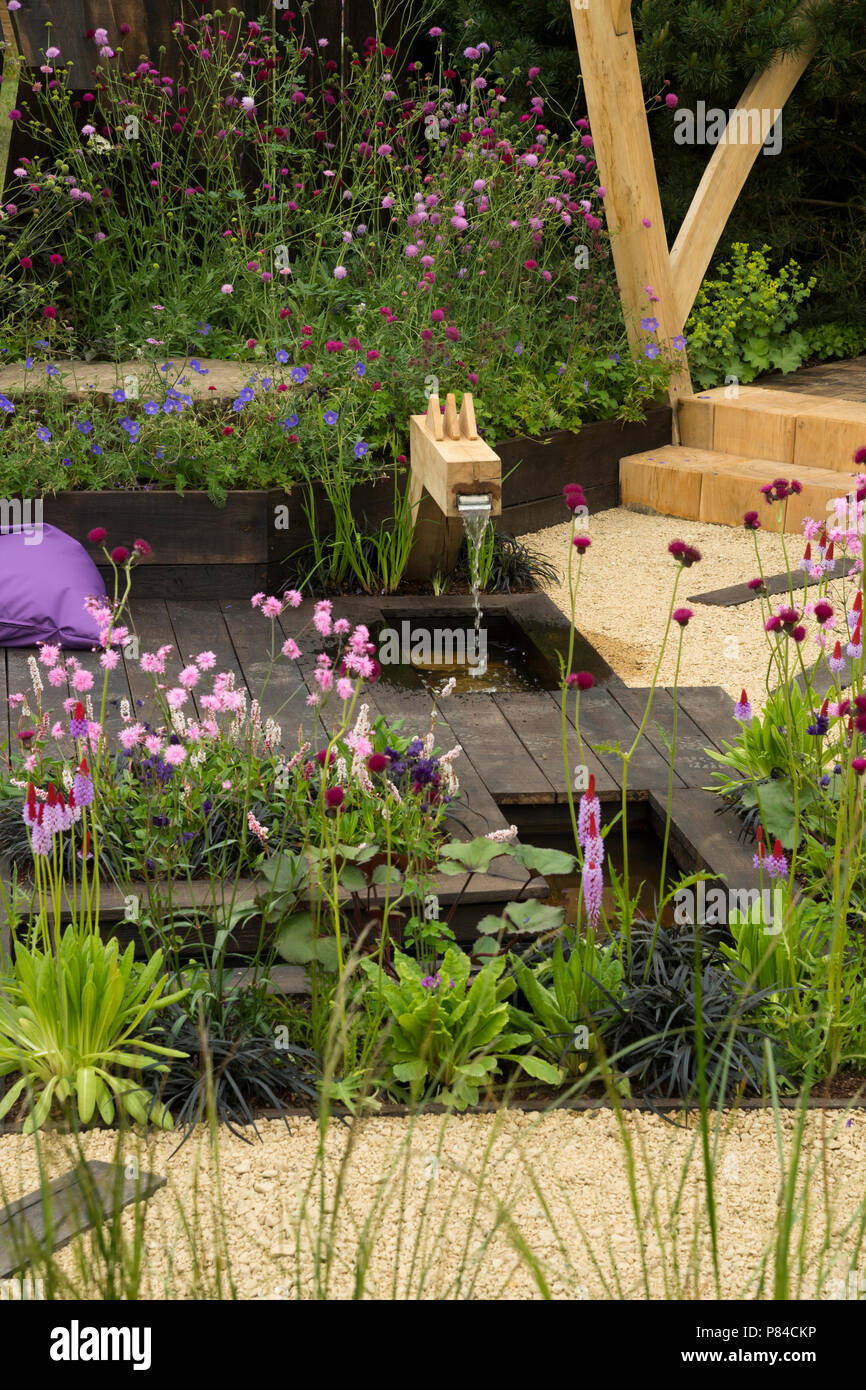 Fiori colorati, stagno & legno beccuccio acqua nella bella prize-winning giardino, i grandi spazi aperti - RHS Chatsworth Flower Show, Inghilterra, Regno Unito. Foto Stock
