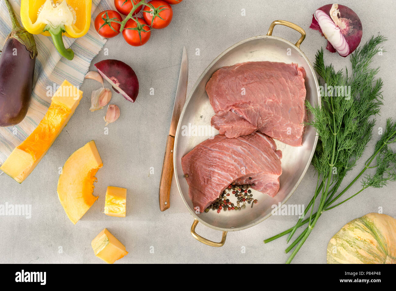 Pezzi di carne di manzo crudo con verdure (zucca, aneto, pepe, pomodori, aglio, melanzana), su una pietra chiara superficie. Ingredienti per la cottura della carne sana Foto Stock