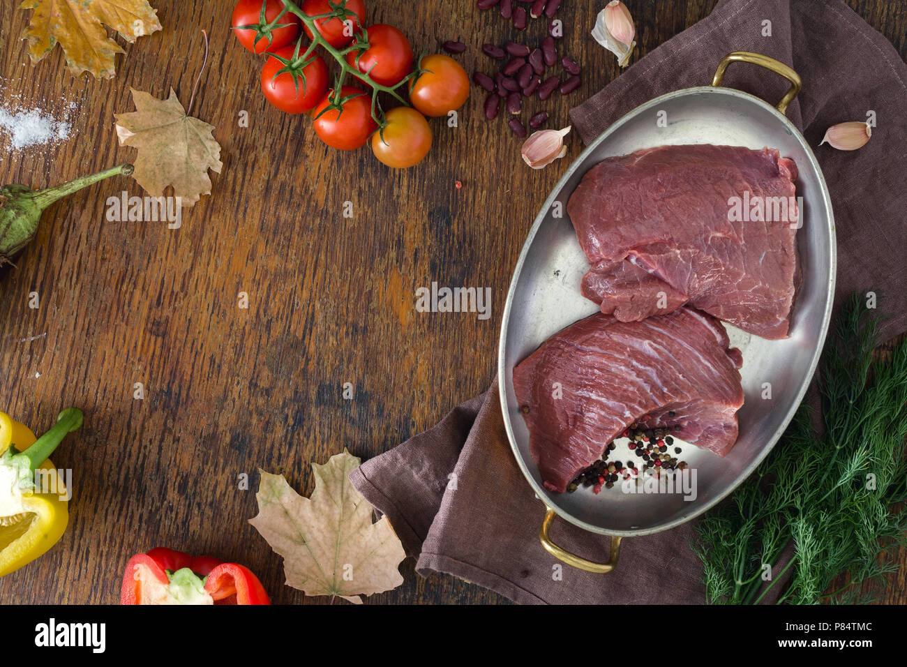 Pezzi di carne di manzo crudo con verdure e foglie di autunno sul tavolo di legno con copia spazio. Ingredienti per la cottura della carne sana la cena. Autunno umore Foto Stock