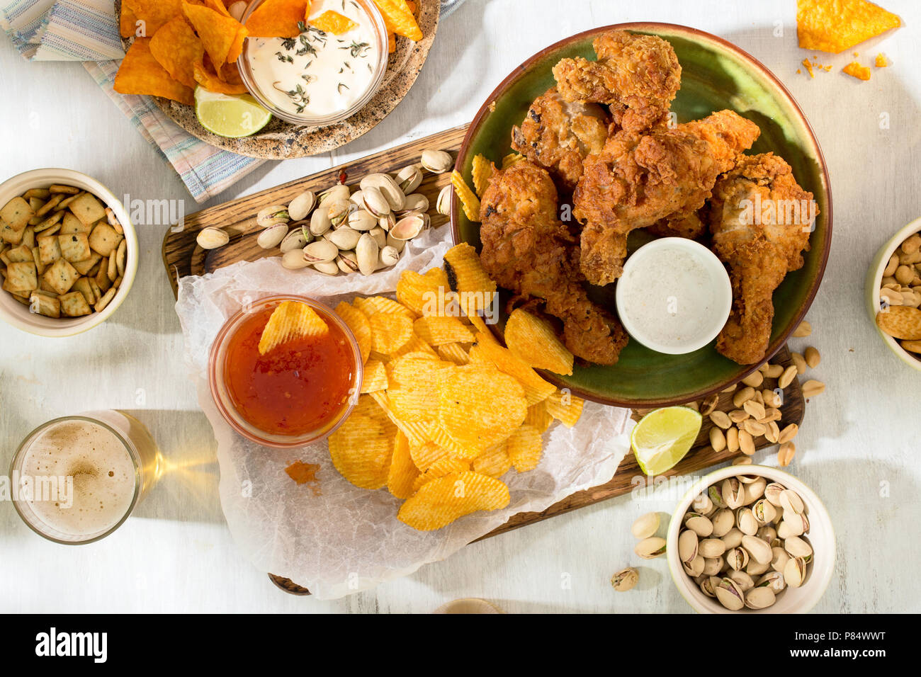 Tabella di partito concetto. Pollo fritto, birra e snack alla birra su di una bianca superficie di legno, vista dall'alto Foto Stock