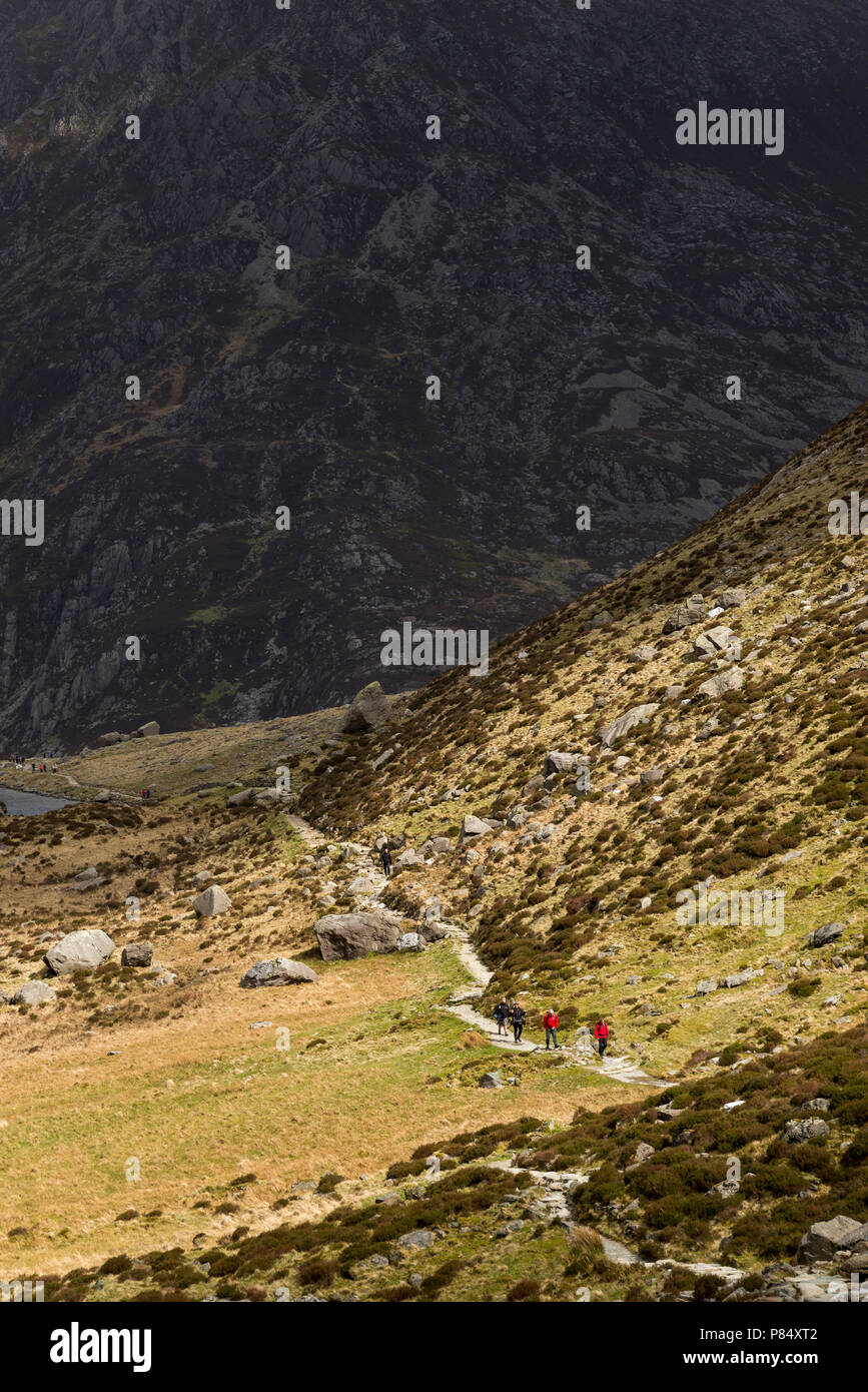 Walkers sul sentiero accanto a Llyn Idwal nel parco nazionale di Snowdonia, Galles. La sfondo montagnoso della penna yr Ole Wen in ombra. Foto Stock