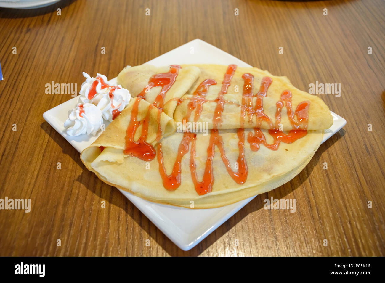 Pancake con sirup di fragole e panna montata in una piastra quadrata Foto Stock