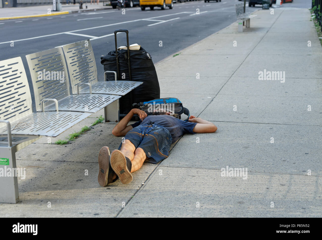 Un uomo senza tetto dormiva sul marciapiede accanto alla sua valigia e zaino sulla via di Hudson in Lower Manhattan. Foto Stock