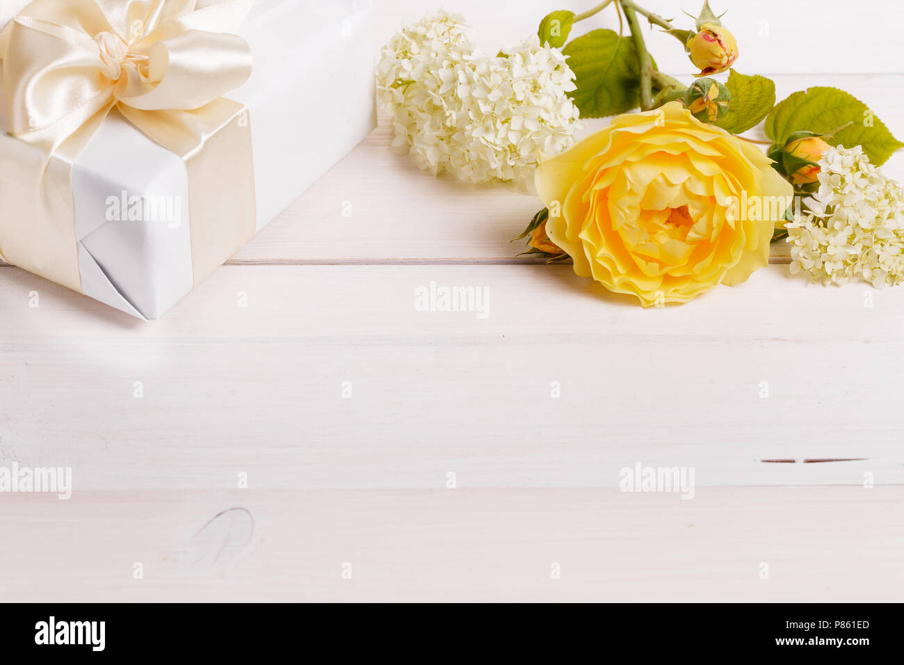 Festosa giallo fiore rosa Inglese e confezione regalo composizione in bianco sullo sfondo di legno. Tettuccio di vista superiore, piatto laici. Copia dello spazio. Compleanno, Madre" Foto Stock