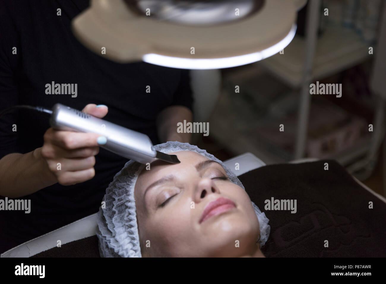 Closeup ritratto di bella donna e la mano con cosmetici dispositivo di sollevamento tocchino il suo volto sotto la lampada Foto Stock