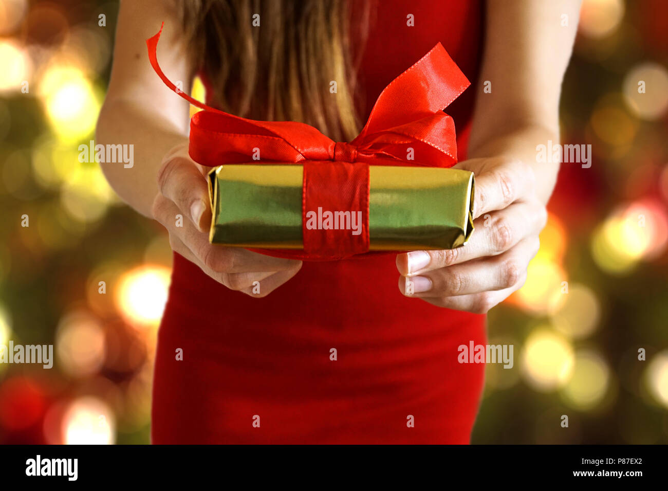 Mani dando carta oro avvolto confezione regalo con un nastro rosso come un presente per Natale Foto Stock