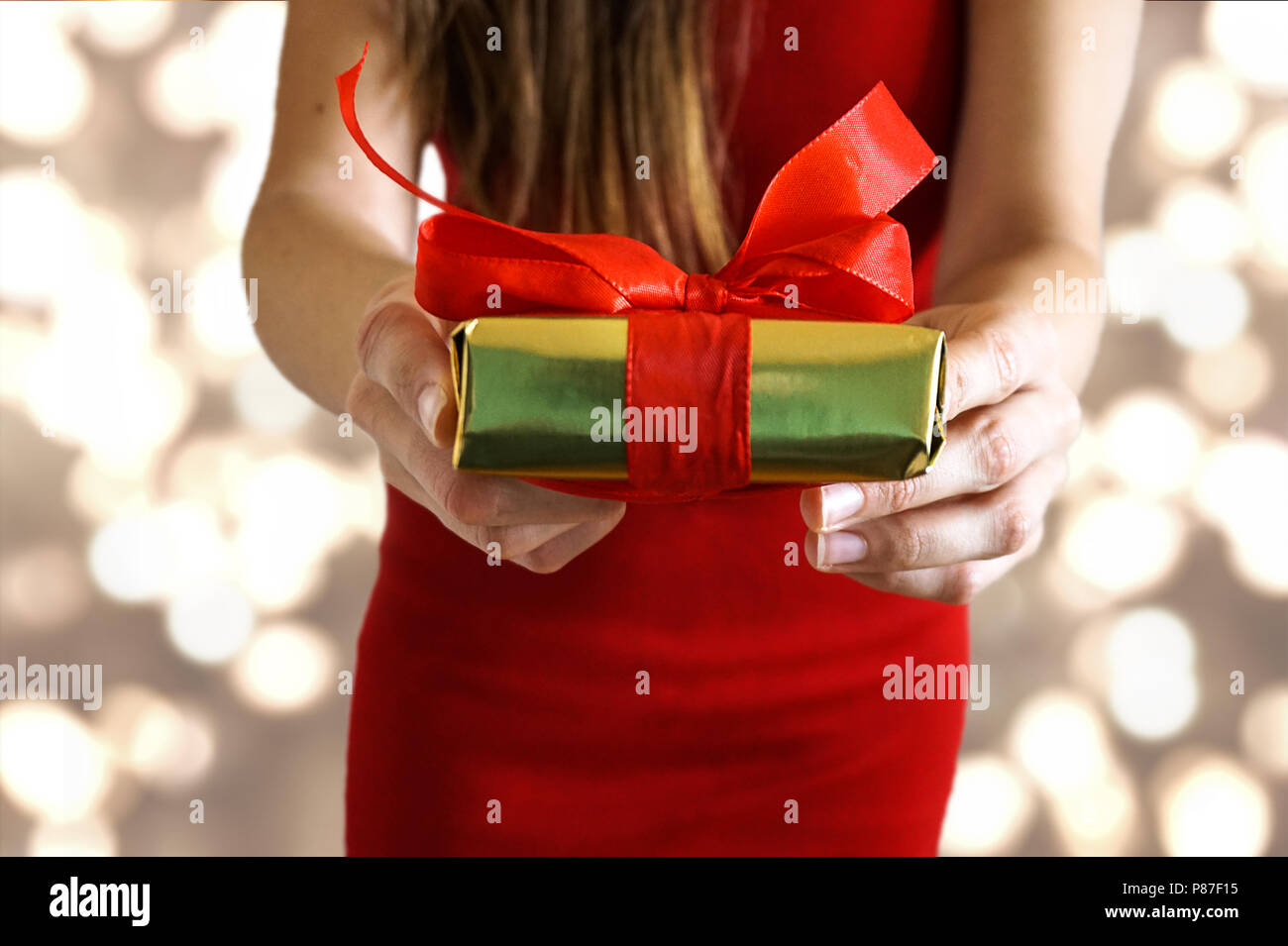 Mani femminili dando un presente con un nastro rosso per il giorno di San Valentino / compleanno /Natale con oro sullo sfondo delle luci Foto Stock