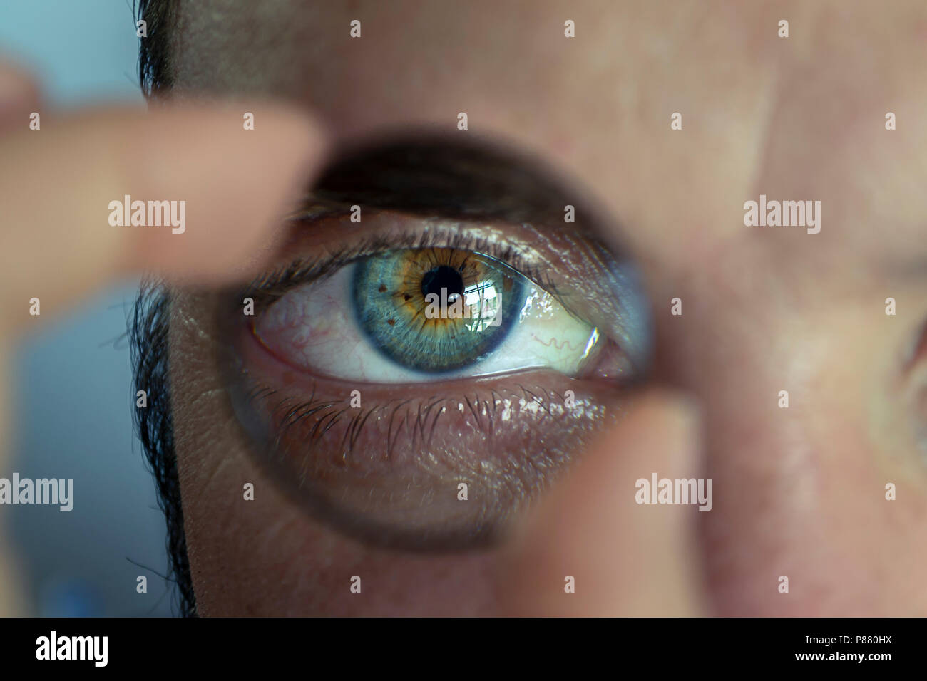 Pimpante uomo ritratto in possesso di una lente di ingrandimento nella parte anteriore del suo occhio Foto Stock