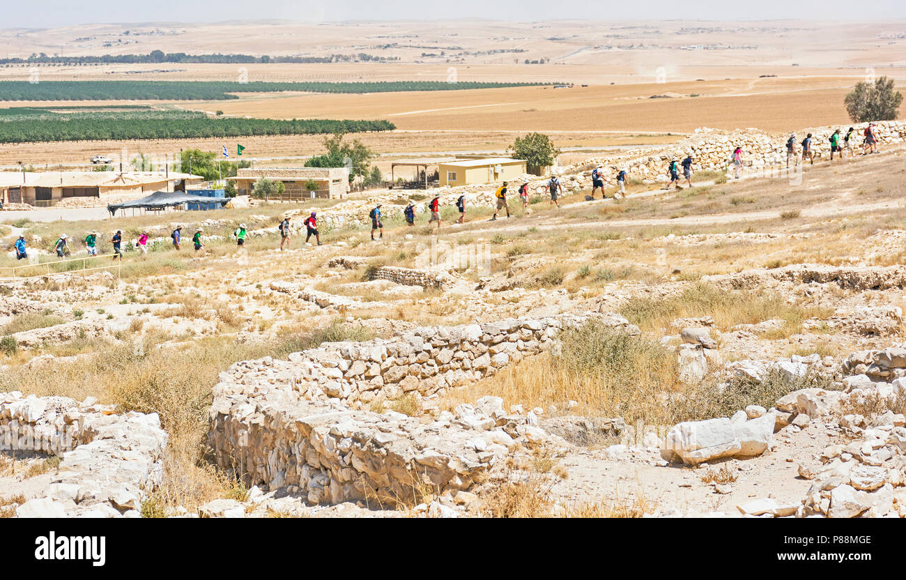 I turisti salendo fino alla antica città cananea a Tel Arad in Israele con una moderna fattoria nel deserto in background Foto Stock