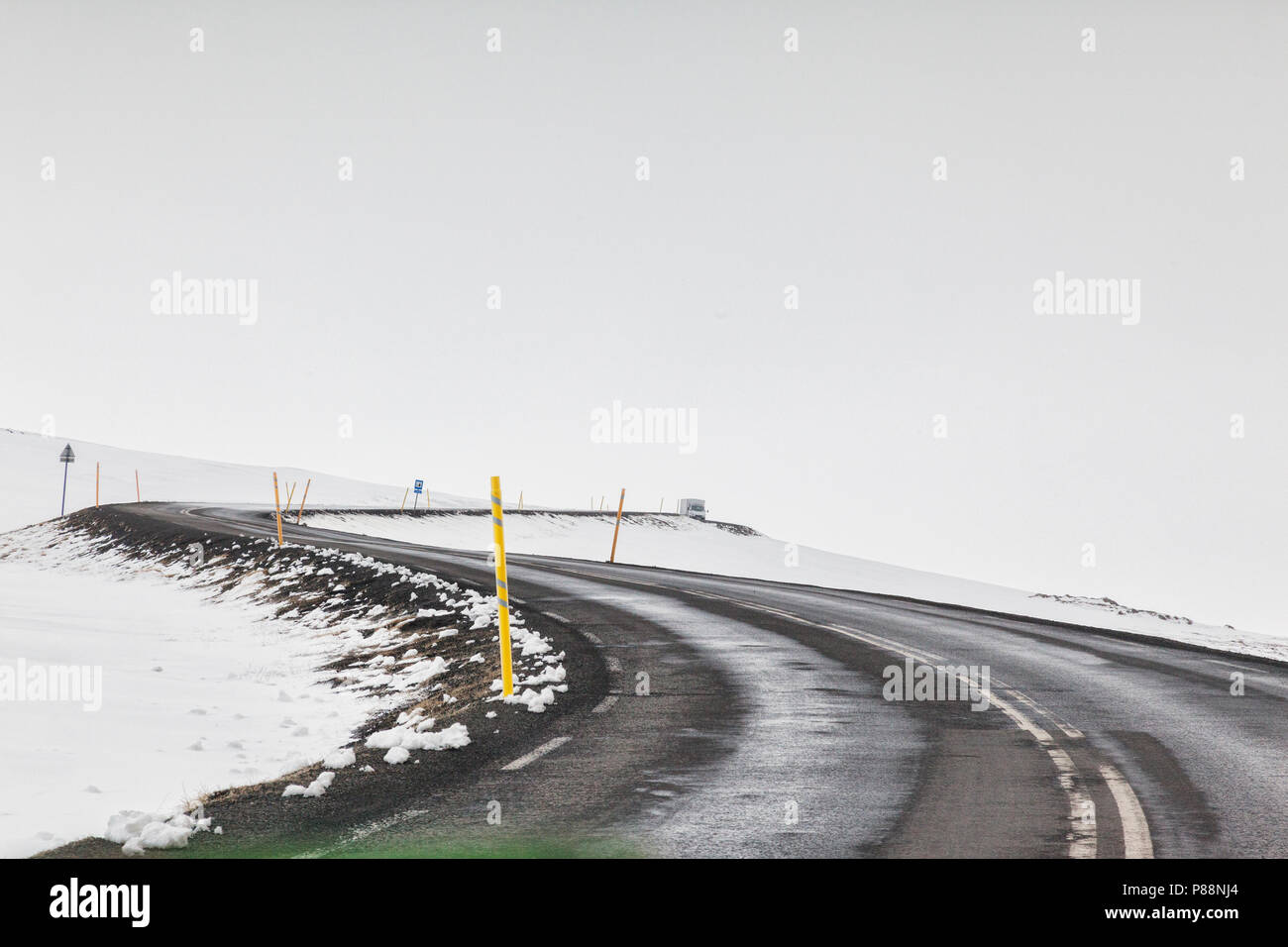 Attraverso il parabrezza colpo di una strada asfaltata in Oriente in Islanda in presenza di nebbia, con una doppia piega e distante un carrello o un autocarro. Foto Stock