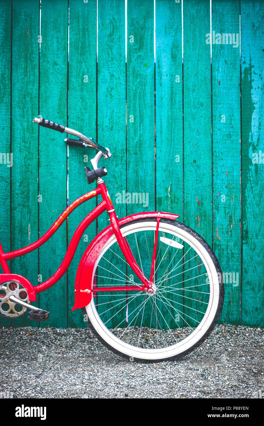 Red vintage in vecchio stile singola velocità bicicletta con pneumatici bianchi appoggiata contro un dipinto di verde staccionata in legno. La British Columbia, Canada. Foto Stock