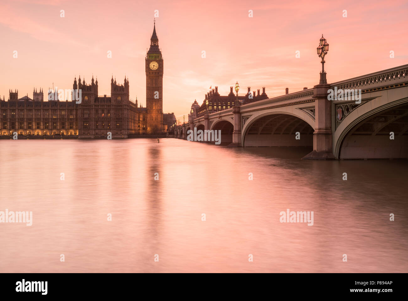Arancione tramonto sul Big Ben e le Camere del parlamento di Londra incluso Westminster Bridge si riflette nell'acqua liscia del Tamigi Foto Stock