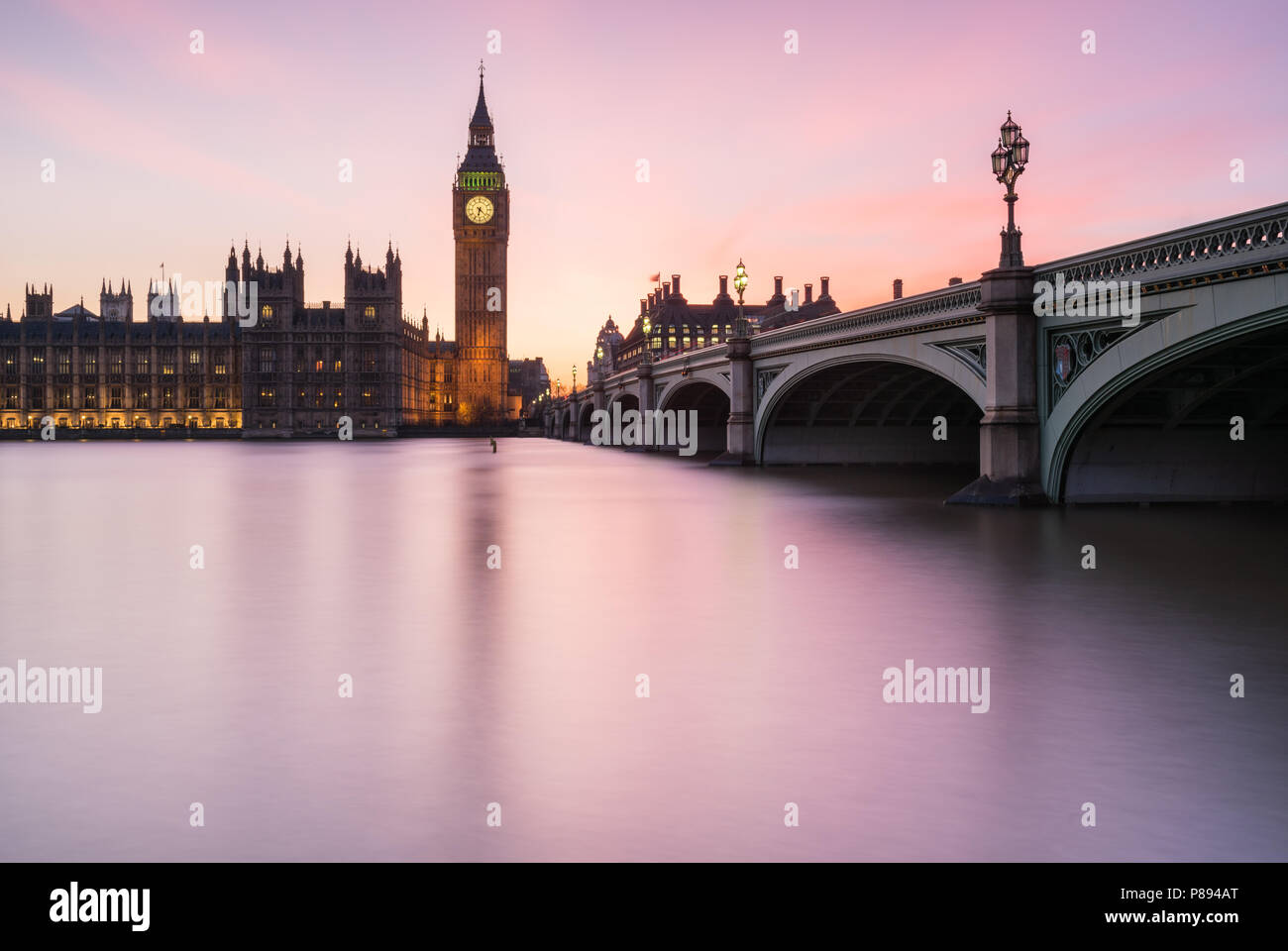 Magenta tramonto sopra il Big Ben e il Parlamento di Londra incluso Westminster Bridge si riflette nell'acqua liscia del Tamigi Foto Stock