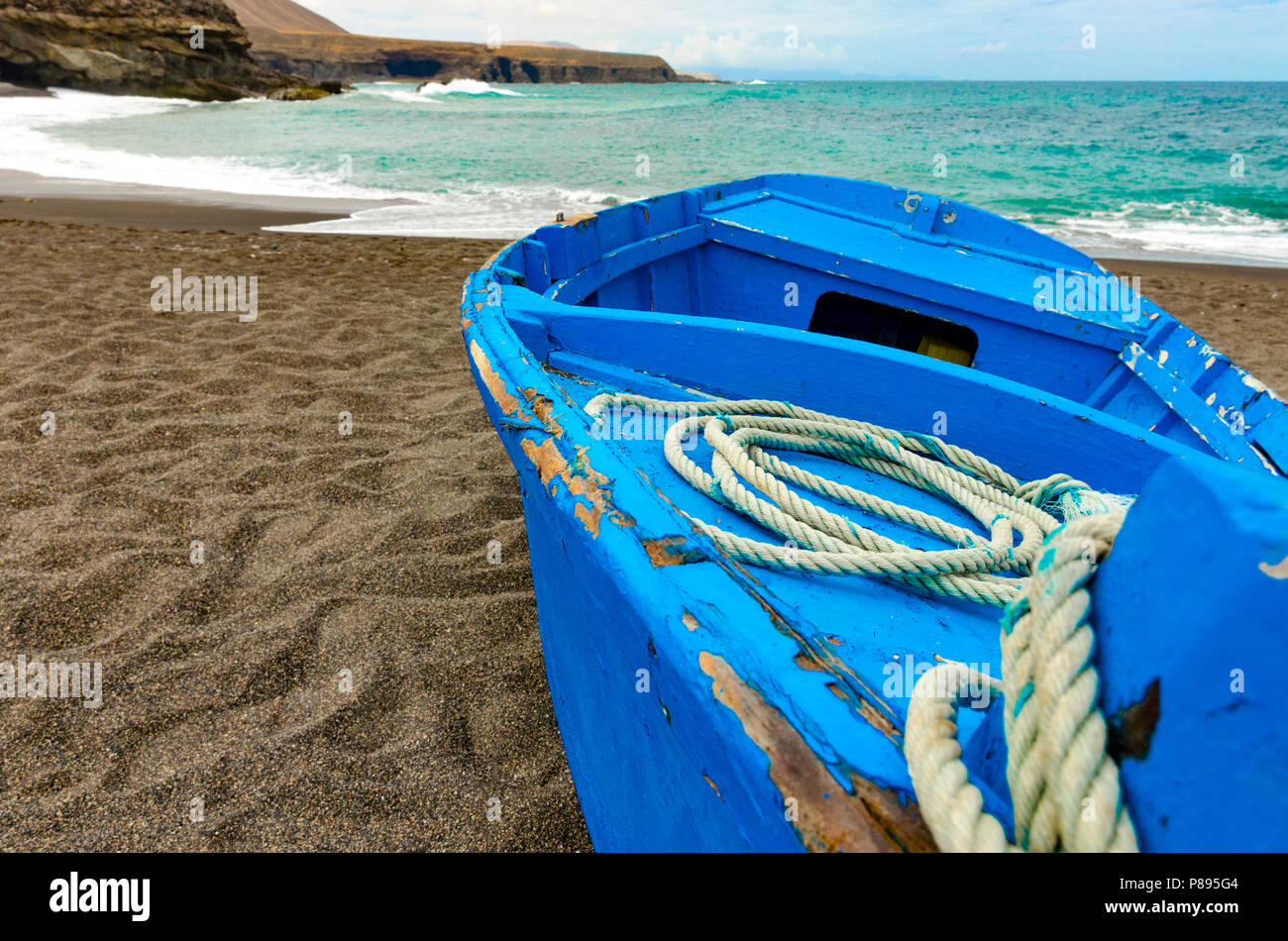 Una vecchia barca blu con una bobina di corda sul nero spiaggia vulcanica Foto Stock