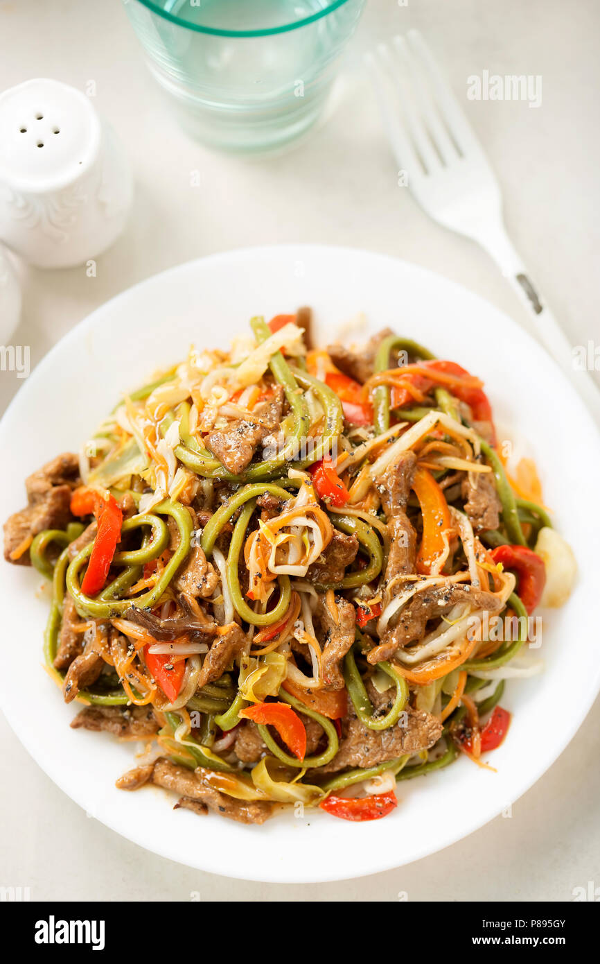 Peperoncino tagliatelle di manzo. Wok fritto in carni bovine il tamarindo e la salsa di soia con tagliatelle verdi, i germogli di soia, carote e peperoni rossi Foto Stock